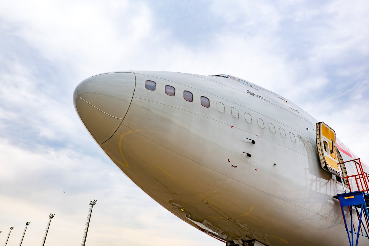 Detailed view of a commercial airplanes nose with an open hatch under a vibrant sky.